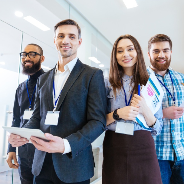 A group of four professionals stands together in a modern office, each wearing ID badges and engaged in conversation