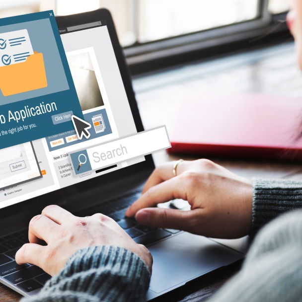 A person types on a laptop, navigating a job application website with a Search bar and clickable buttons visible on the screen