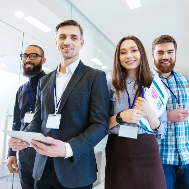 A group of four professionals stands together in a modern office, each wearing ID badges and engaged in conversation